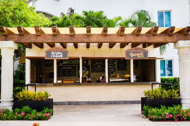 Barefoot restaurant counter with wooden pergola, palm trees, and blue door entrance