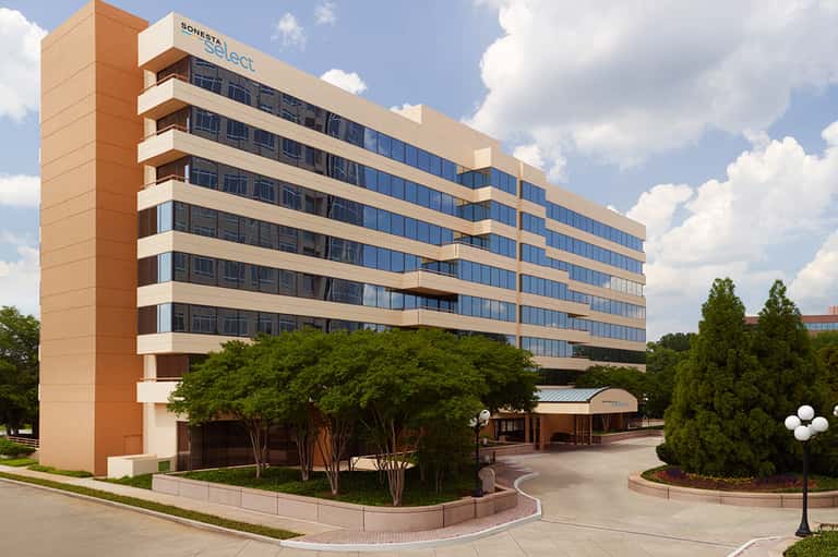 Sonesta Select hotel, multi-story tan and white building with tree landscaping and modern architecture