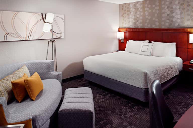 Modern hotel bedroom with red accent headboard, gray sofa, and contemporary furnishings