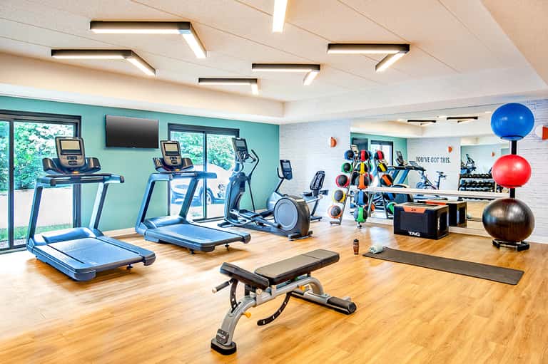 Bright fitness center with treadmills, exercise equipment, and turquoise accent wall