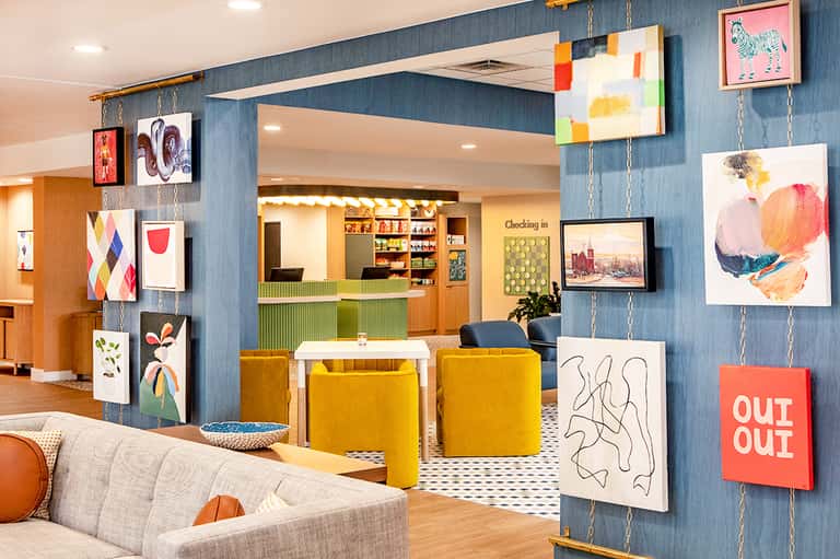 Modern hotel lobby with colorful artwork, blue accent wall, yellow seating, and check-in desk