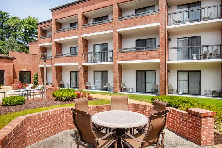 Red brick apartment building courtyard with round table, wicker chairs, and manicured landscaping