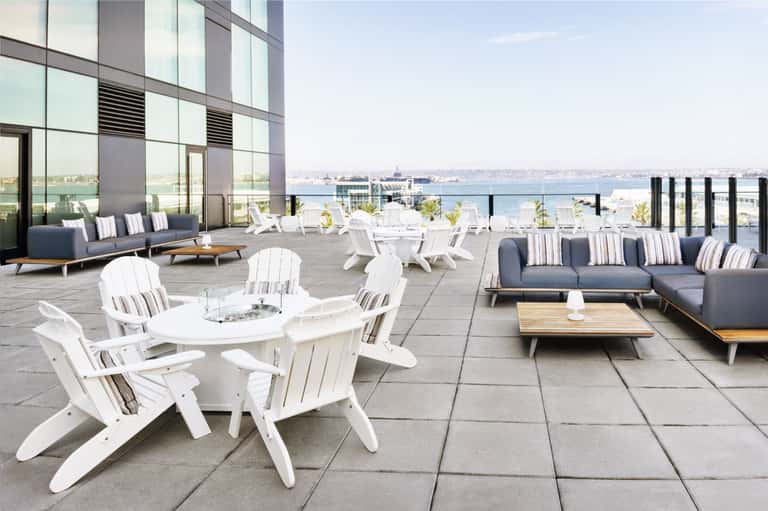 Rooftop terrace with white Adirondack chairs, modern seating areas, and waterfront city views