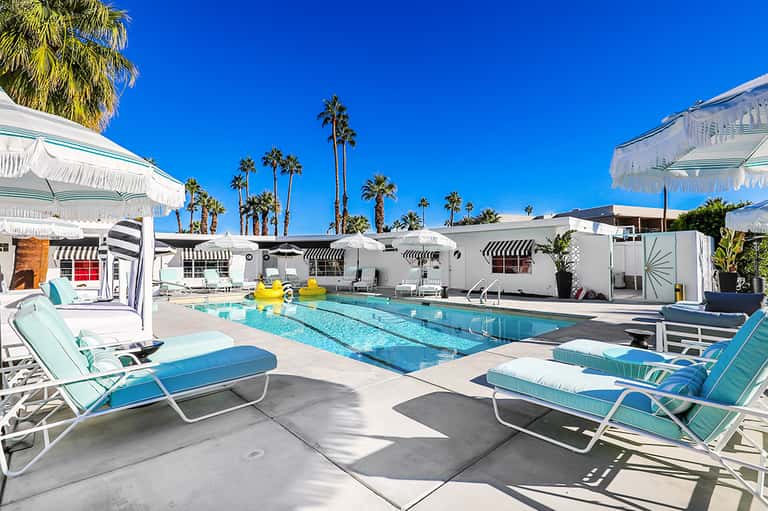 Modern resort pool with lap lanes, turquoise lounge chairs, white umbrellas, and palm trees