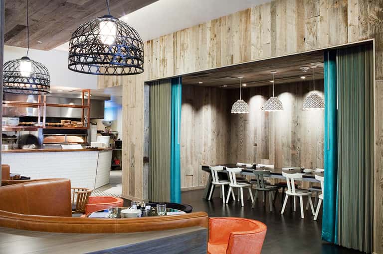 Modern hotel restaurant and bar with pendant lighting, wood walls, and turquoise accents