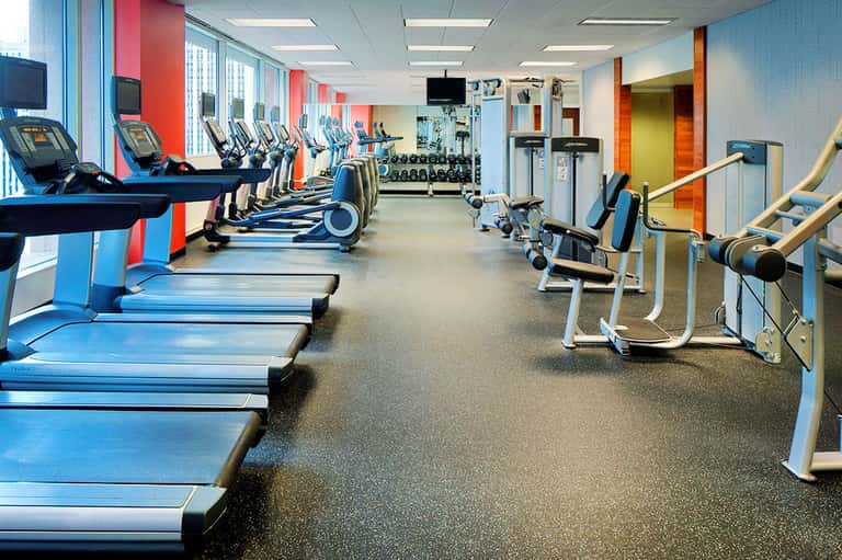 Spacious fitness center with rows of treadmills, colorful accent walls in red and blue, and exercise equipment