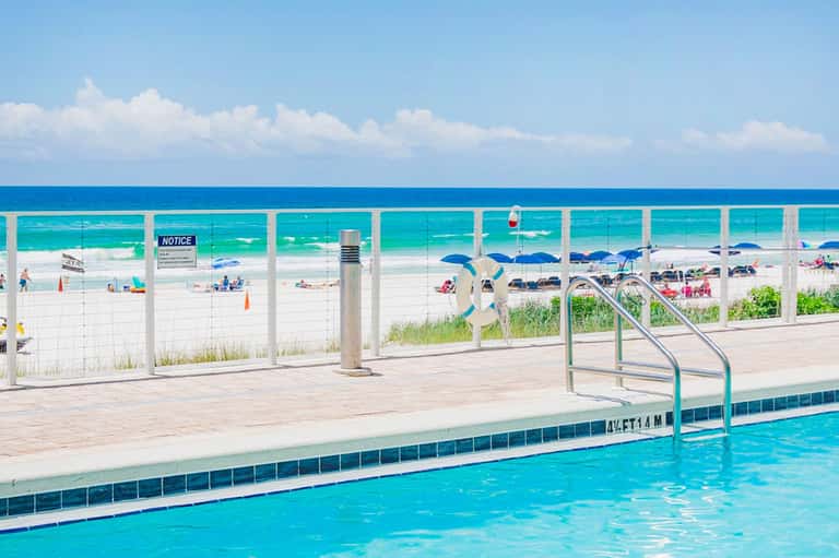 Outdoor swimming pool with ocean view and beach access behind white safety fencing