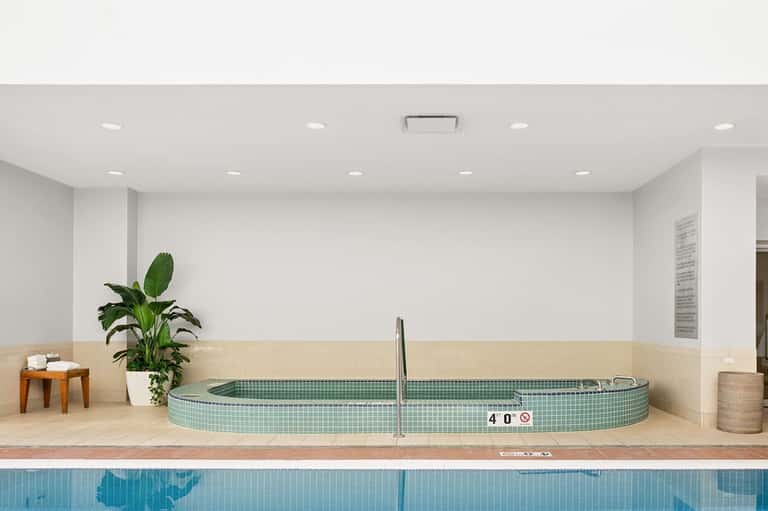 Spa soaking tub with green tile interior next to indoor lap pool with depth marker