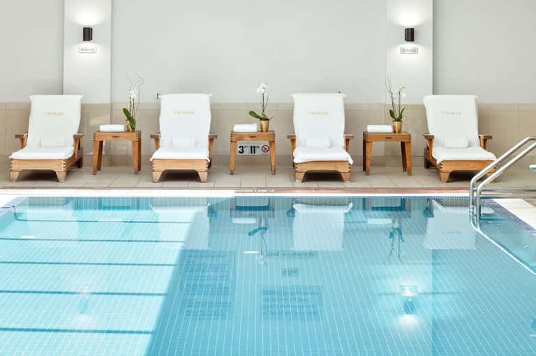 Indoor lap pool with Conrad-branded lounge chairs and potted flowers along the edge