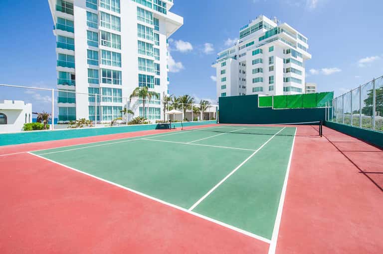 Rooftop tennis court with high-rise residential buildings and palm trees in background