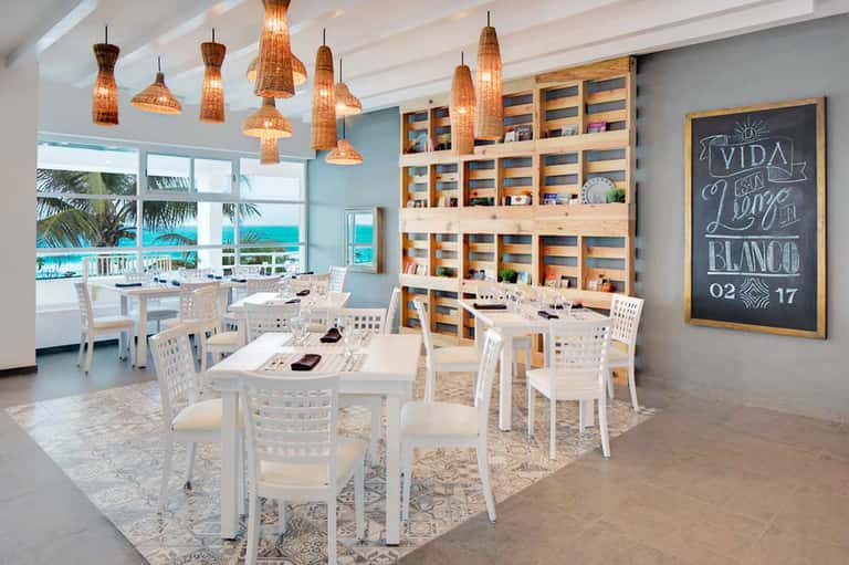 Bright beachfront restaurant with ocean views, woven pendant lights, and casual dining setup