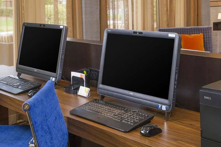 Hotel business center with desktop computers, wooden desk, and window with outdoor views