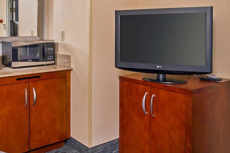 Hotel room kitchenette with microwave, television, and wooden cabinetry