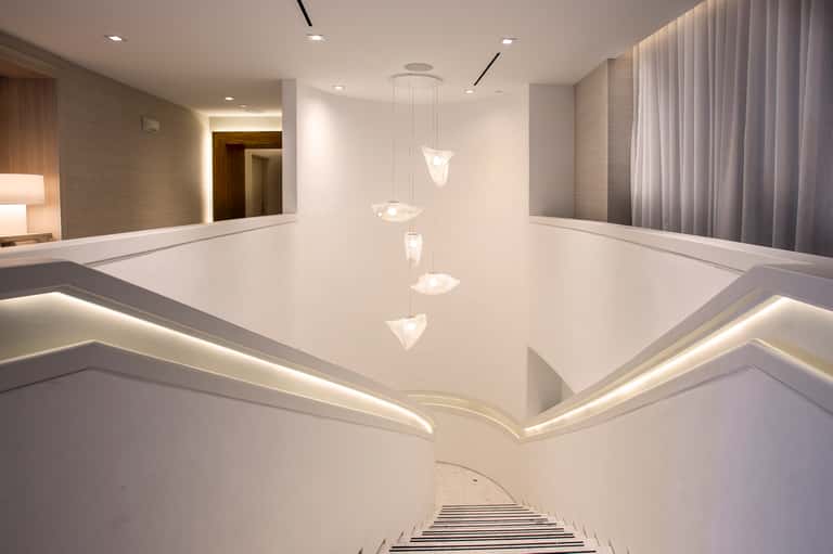 Modern hotel hallway with white walls, pendant lighting, mirrors, and contemporary architectural design