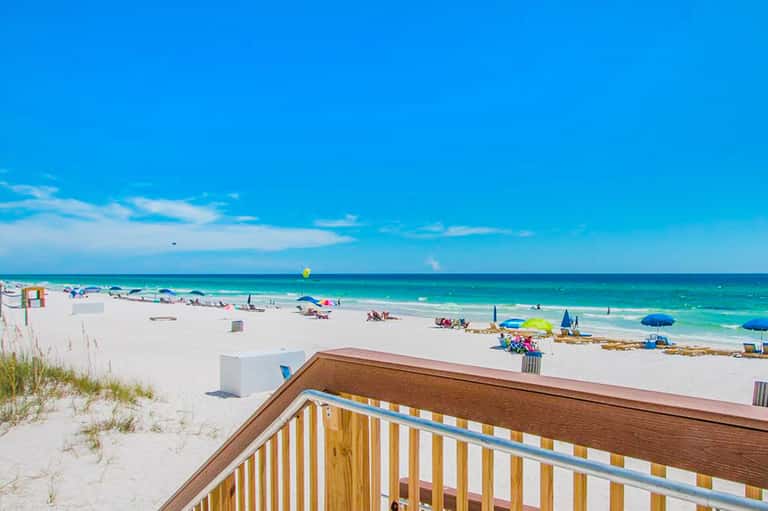 Pristine sandy beach with colorful umbrellas and clear turquoise water viewed from beachfront deck railing