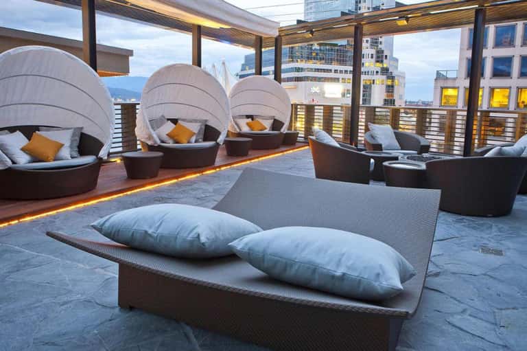 Modern rooftop lounge with pod-style seating, white cushions, and city skyline views