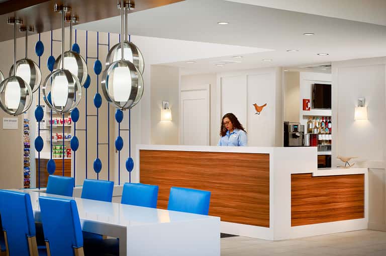 Modern hotel reception desk with blue chairs, decorative metal pendant lights, and wooden accents