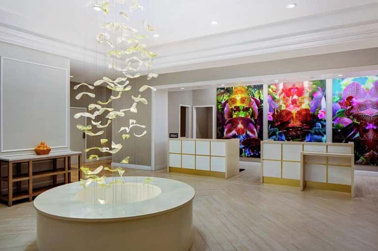 Modern resort lobby with sculptural pendant lighting, orchid artwork displays, and marble surfaces