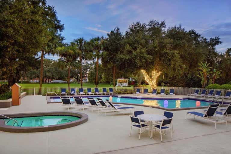 Resort pool at dusk with spa tub, loungers, and illuminated trees in background