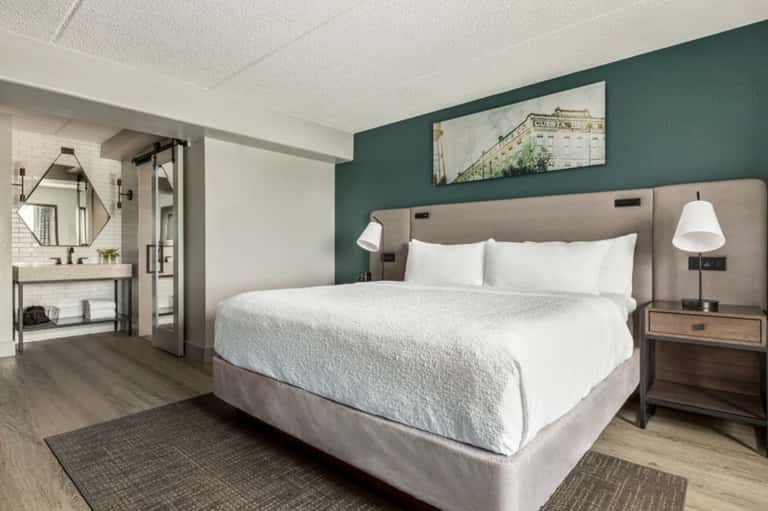 Modern hotel bedroom with queen bed, green accent wall, and en-suite bathroom
