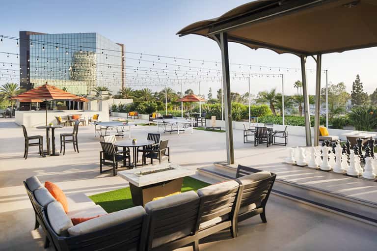 Modern resort rooftop terrace with dining tables, fire pit, and city skyline views