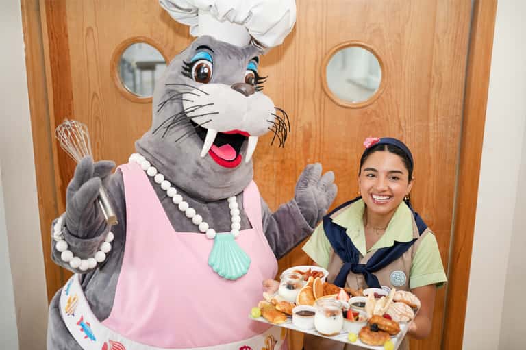 Character mascot chef with woman holding pastry plate near ship interior porthole