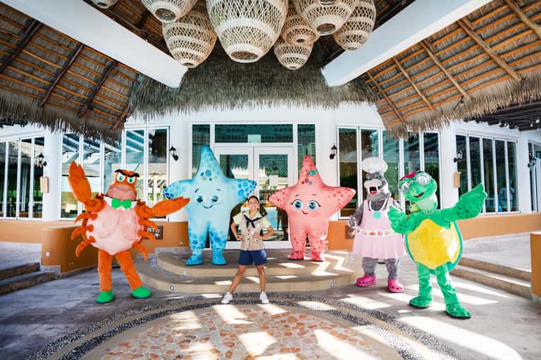 Child posing with colorful sea creature mascots under thatched roof structure