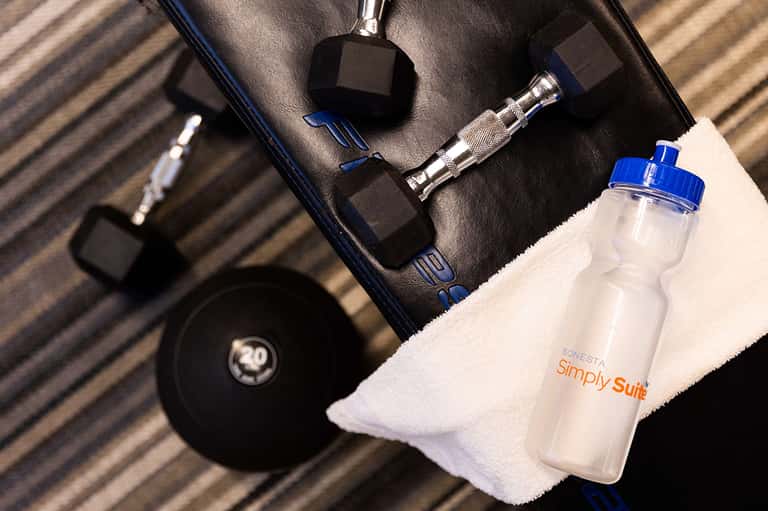 Fitness equipment including dumbbells and water bottle labeled Simply Suite on towel