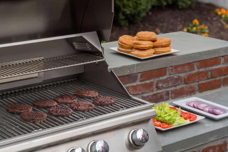 Outdoor grill cooking hamburgers with donuts and fresh vegetables on adjacent counter