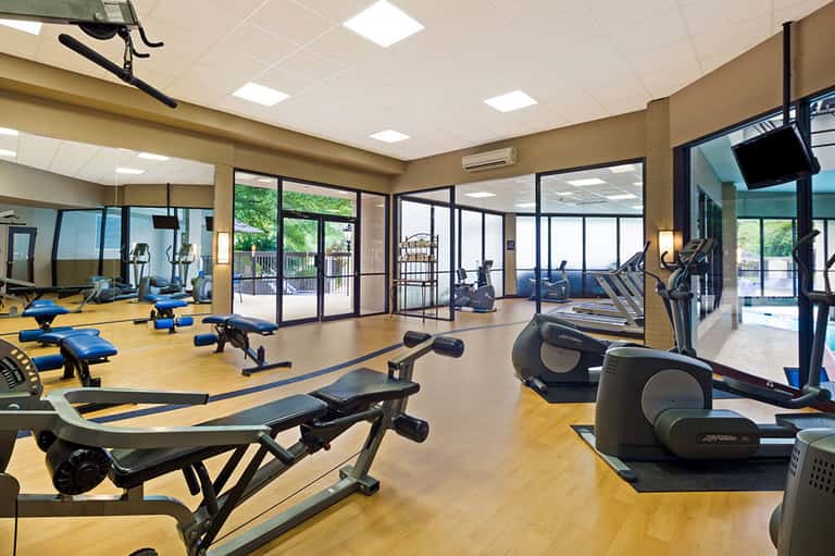 Fitness center with exercise equipment, mirrors, large windows, and outdoor pool view