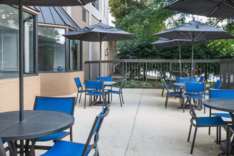 Waterfront patio with blue umbrellas, dining tables, modern railing, trees, and lakefront views