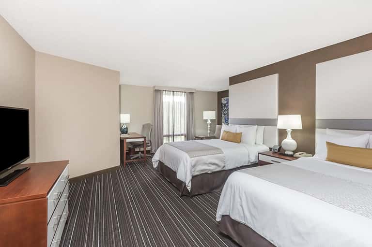 Hotel guest room with two queen beds, desk, and warm neutral decor