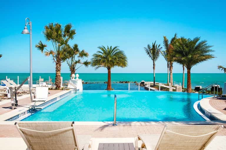 Turquoise infinity pool with palm trees overlooking the ocean and clear blue sky