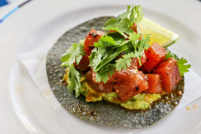 Gourmet tostada appetizer with avocado, tomato, cilantro on gray plate