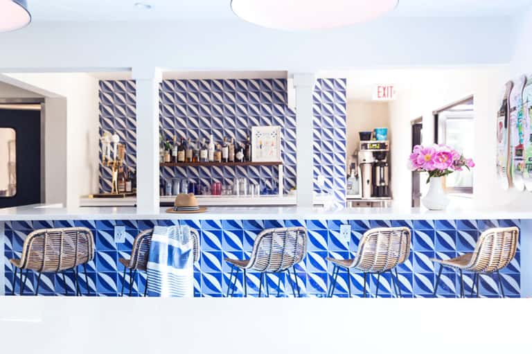 Contemporary bar with blue geometric tile pattern, white rattan stools, and shelved liquor display