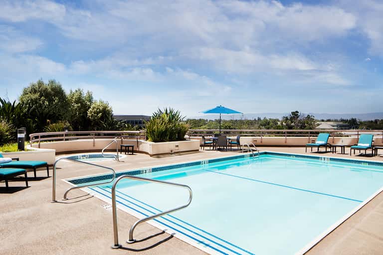 Resort pool with blue umbrella, lounge chairs, and mountain views in background