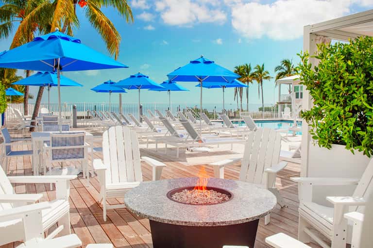 Beachfront deck with blue umbrellas, white adirondack chairs, and a fire pit overlooking the ocean