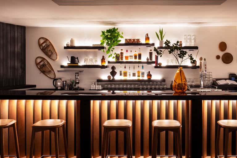 Modern spa bar with black counter, wooden stools, and illuminated shelving display