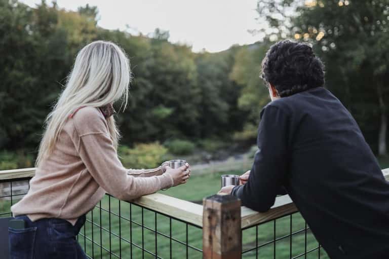 Two people enjoying drinks on a scenic overlook with forested landscape