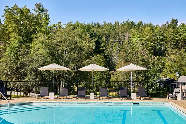 Olympic-style lap pool with three white umbrellas and forest backdrop in daylight