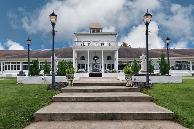 Grand white columned building with dome, flanked by manicured lawn, black lamp posts, and classical architecture