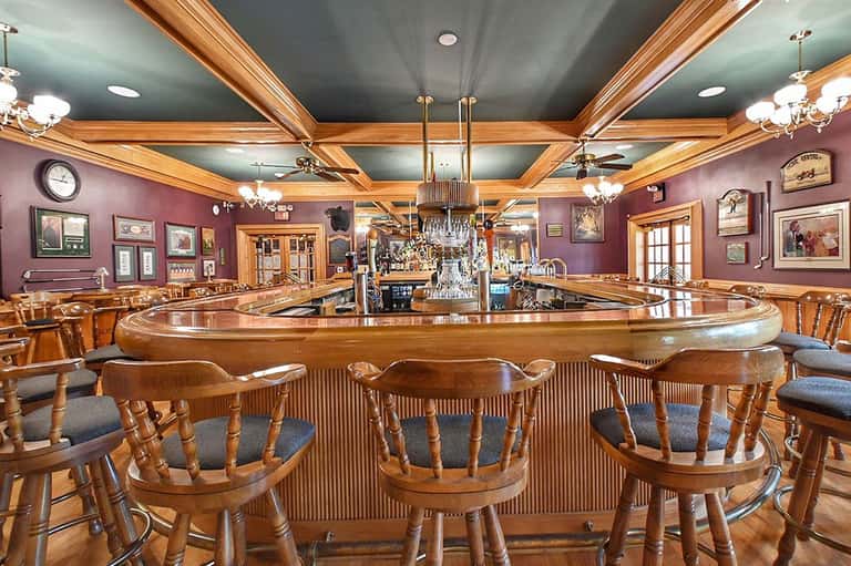 Elegant wooden bar with purple walls, chandeliers, and wood-paneled ceiling