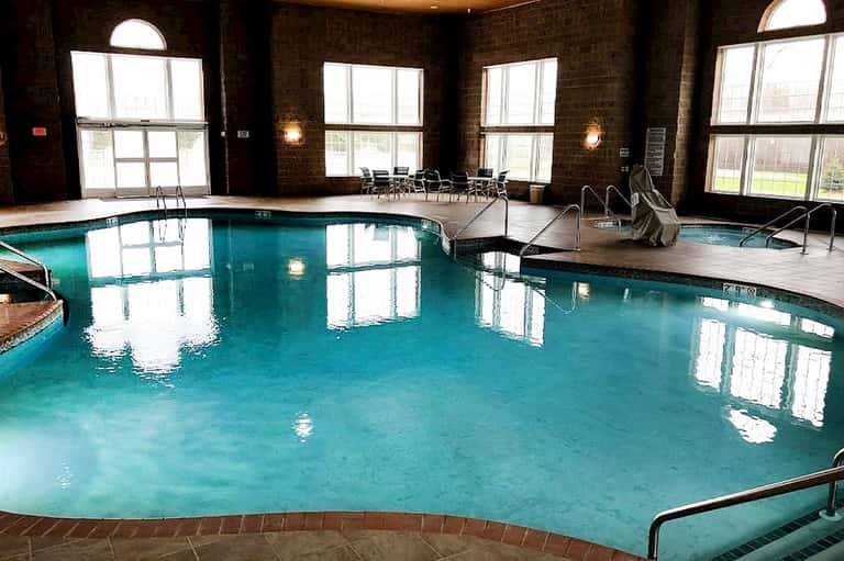 Indoor swimming pool facility with turquoise water, large windows, lounging area, and modern architecture
