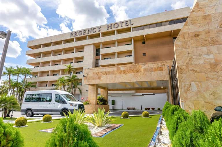 Regency Hotel exterior with stone facade, palm trees, manicured lawn, and shuttle van parked outside