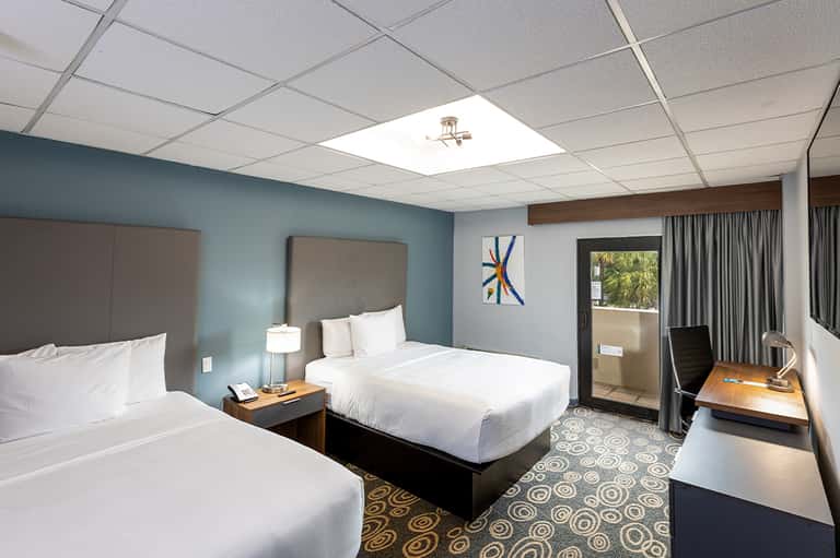Hotel room with two queen beds, blue walls, desk area, and sliding glass door