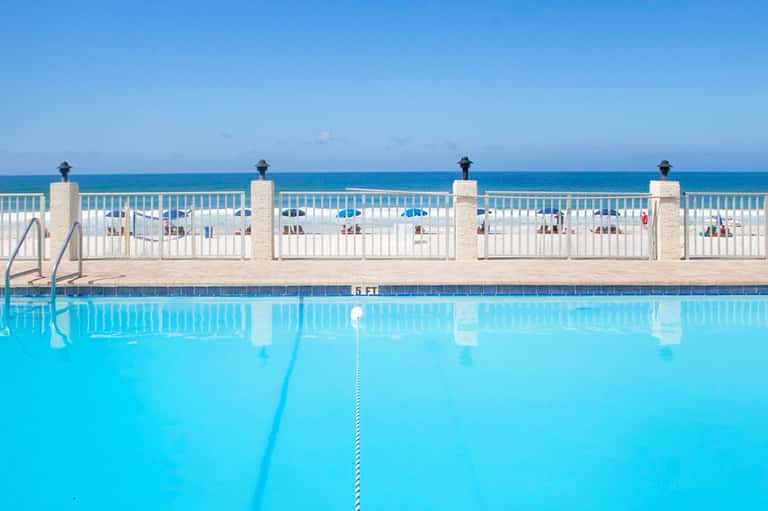 Olympic-length swimming pool with lane dividers overlooking the ocean and beach with umbrellas