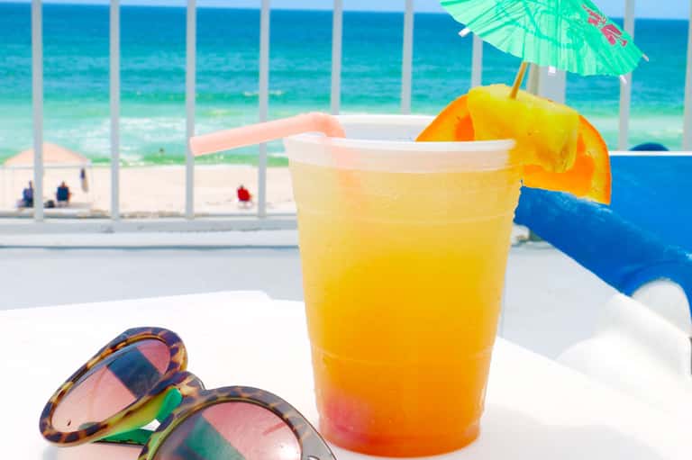 Tropical cocktail with orange slice and umbrella on beachside table overlooking ocean