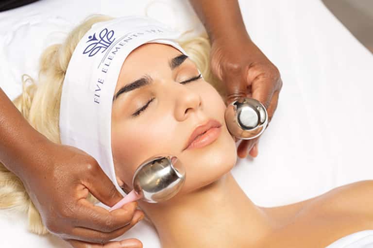 Spa facial treatment with therapist applying metal cooling spheres to client's face wearing headband