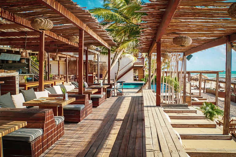 Wooden beachfront pavilion with lounge seating, palm trees, and ocean view at tropical resort