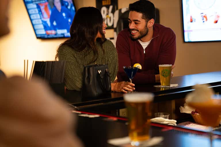 Couple enjoying drinks at bar counter with sports displays and casual indoor resort atmosphere